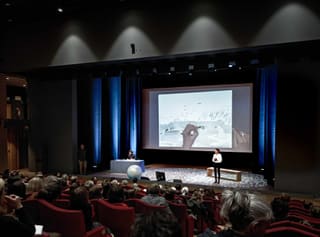 Hugo Letellier sur scène devant une salle comble, une illustration polaire projetée sur grand écran.